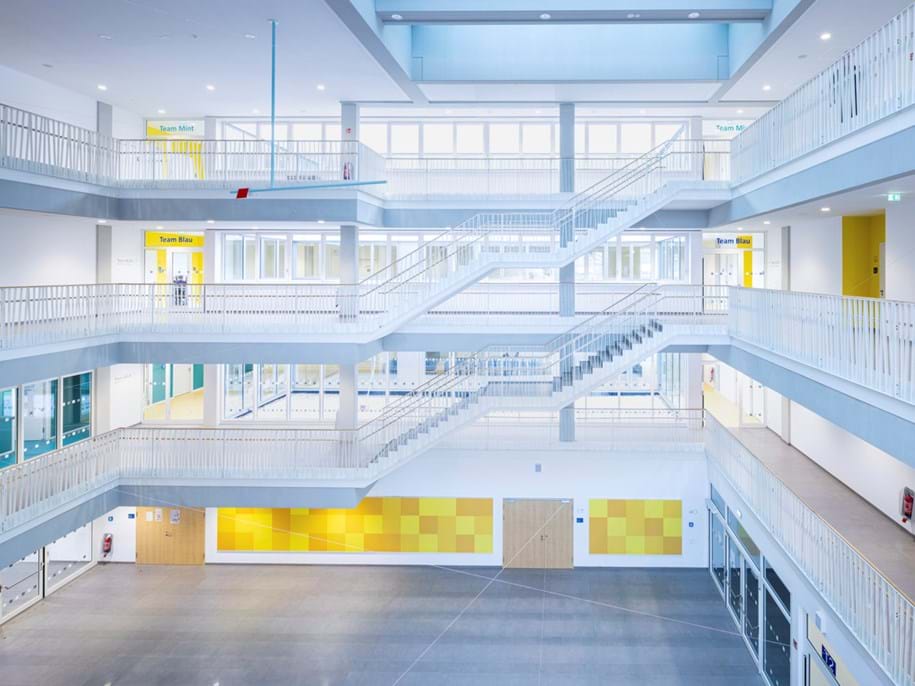 White acoustic ceiling in spacious atrium with staircases and yellow details on the walls