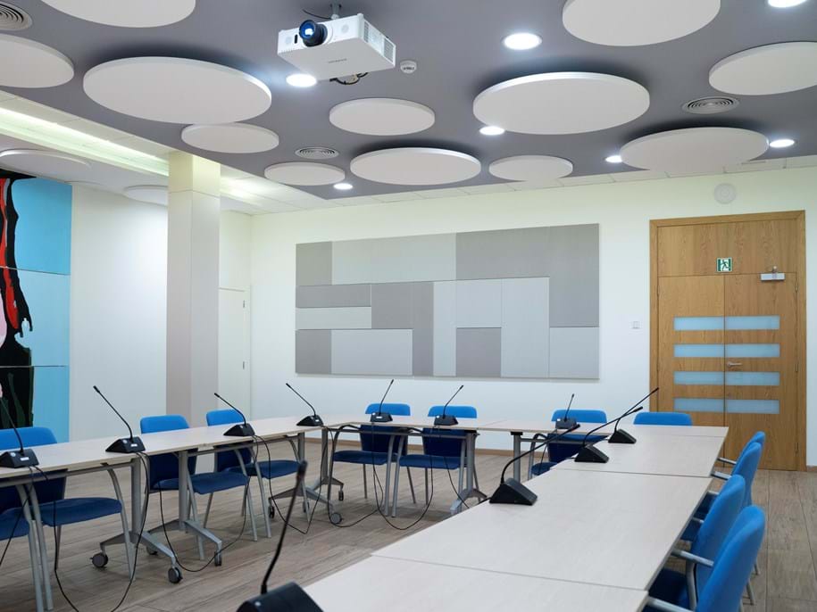 Large conference room with a U-shaped seating arrangement, grey acoustic wall panels in a pattern and white circle shaped free-hanging ceiling panels.