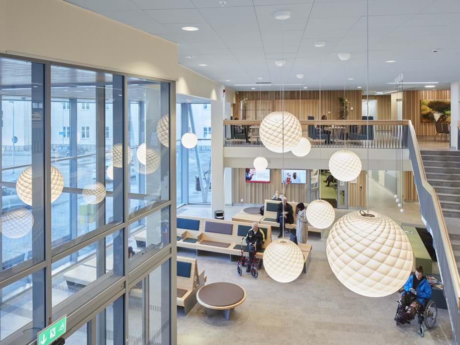 White, suspended acoustic ceiling in spacious hospital entrance with a seating area and a staircase leading up to the first floor