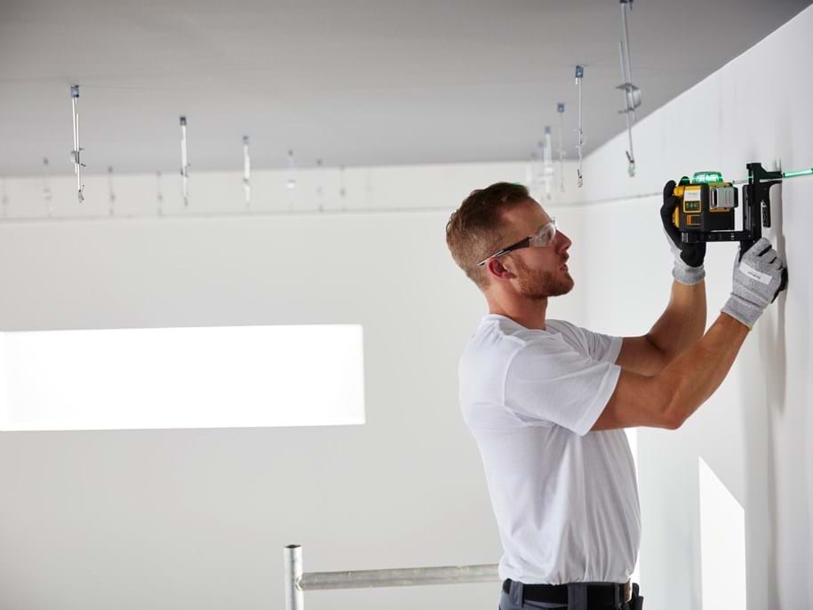 Installer measuring an empty room preparing for ceiling installation