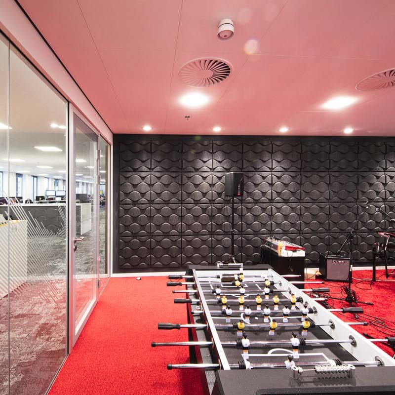 Pink, suspended acoustic ceiling in office game and music room with red carpet and black wall decorations