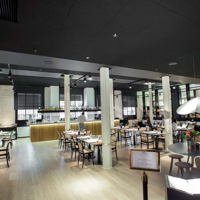 Black, suspended acoustic ceiling in restaurant with bar surrounded by tables and chairs